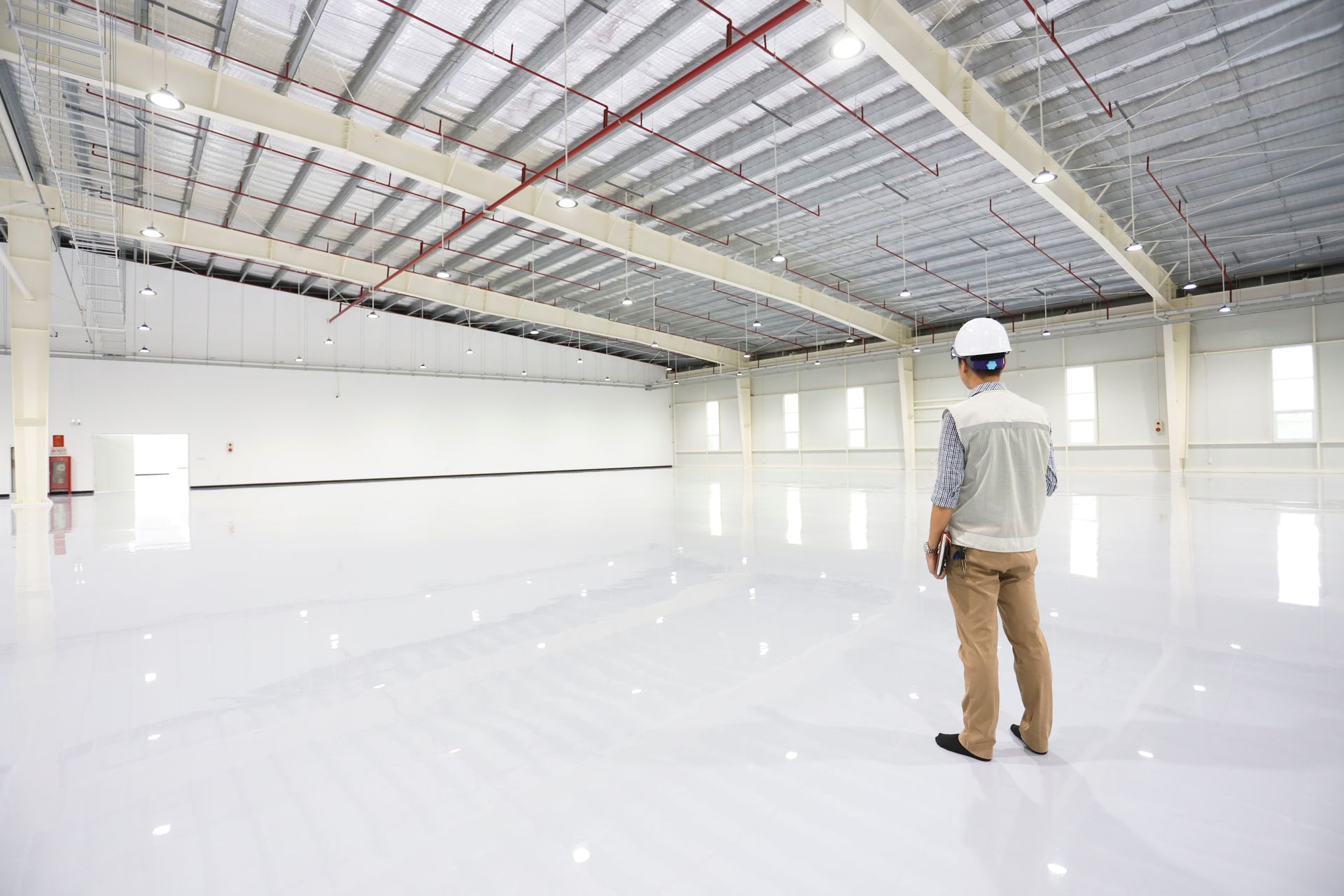 Man in hard hat stands in a large, empty warehouse with bright white floors and walls.