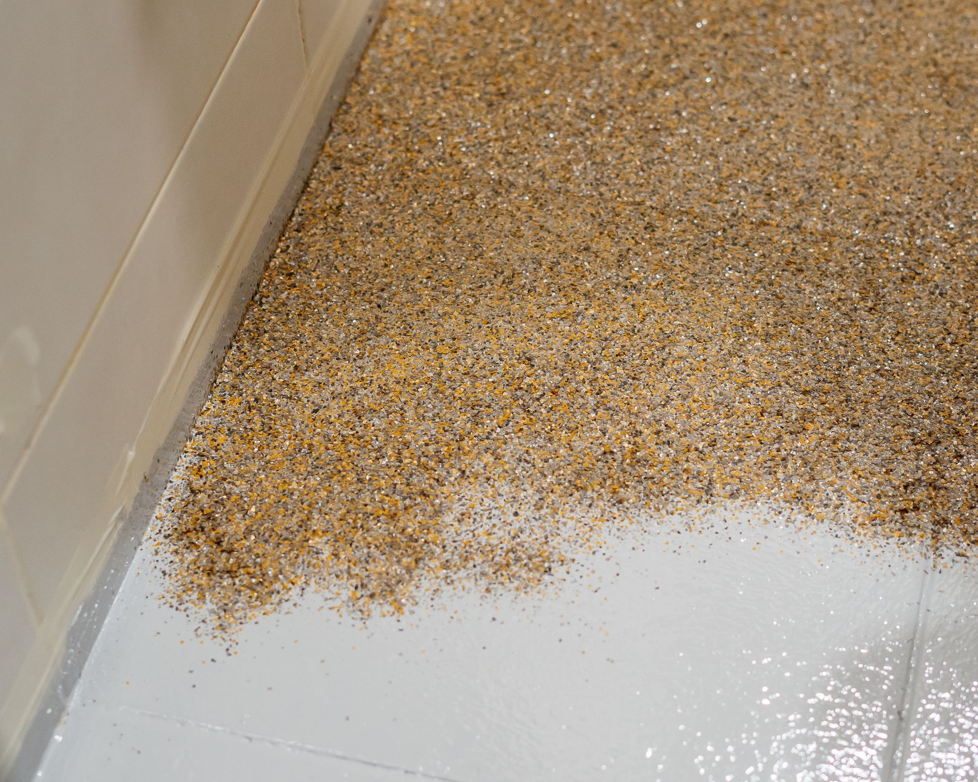 Gravelly, beige surface covering a floor next to a white wall.