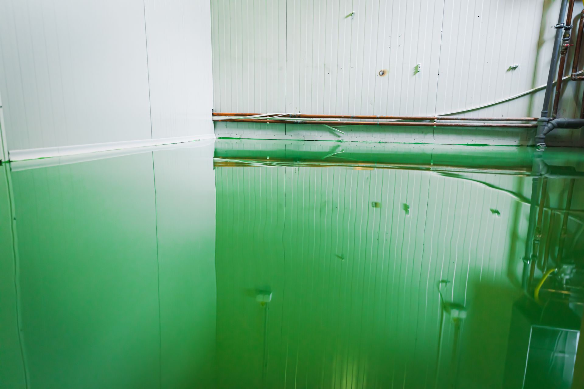 Green liquid spills across a room with white walls, creating reflections.