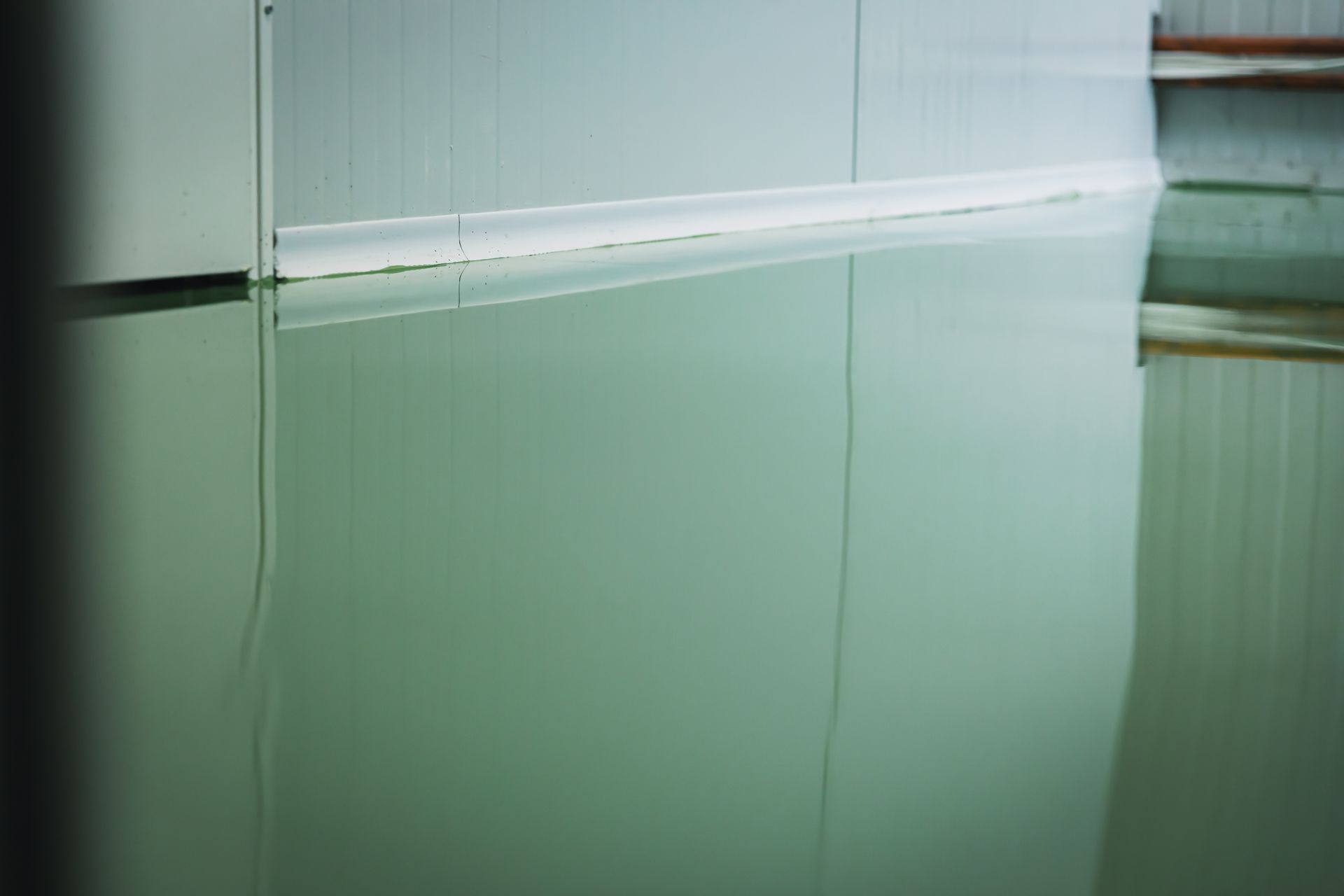 Reflective, green-toned epoxy floor with a light-colored wall reflected in it.