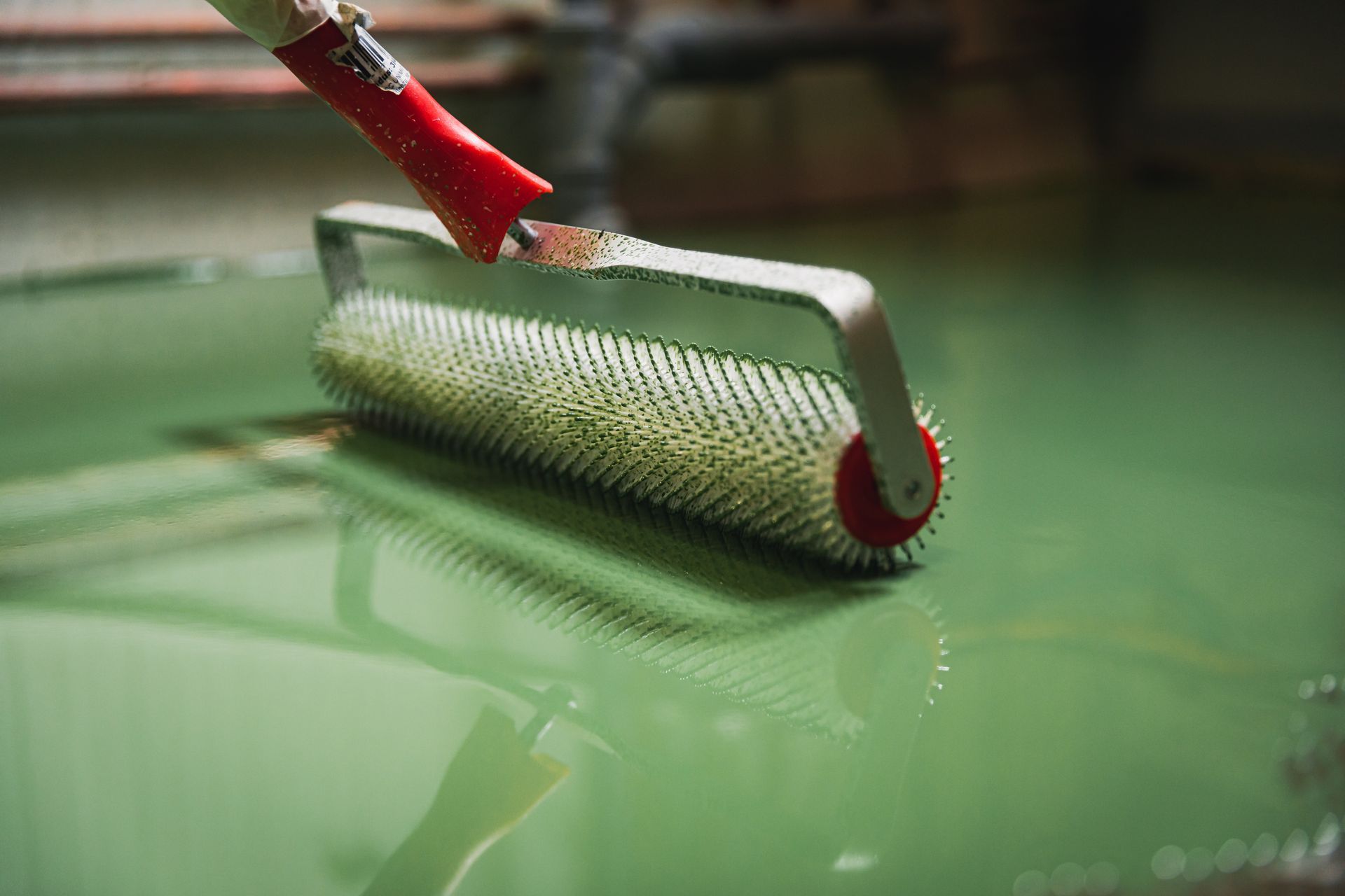 A green floor being leveled with a spiked roller; red handle visible.