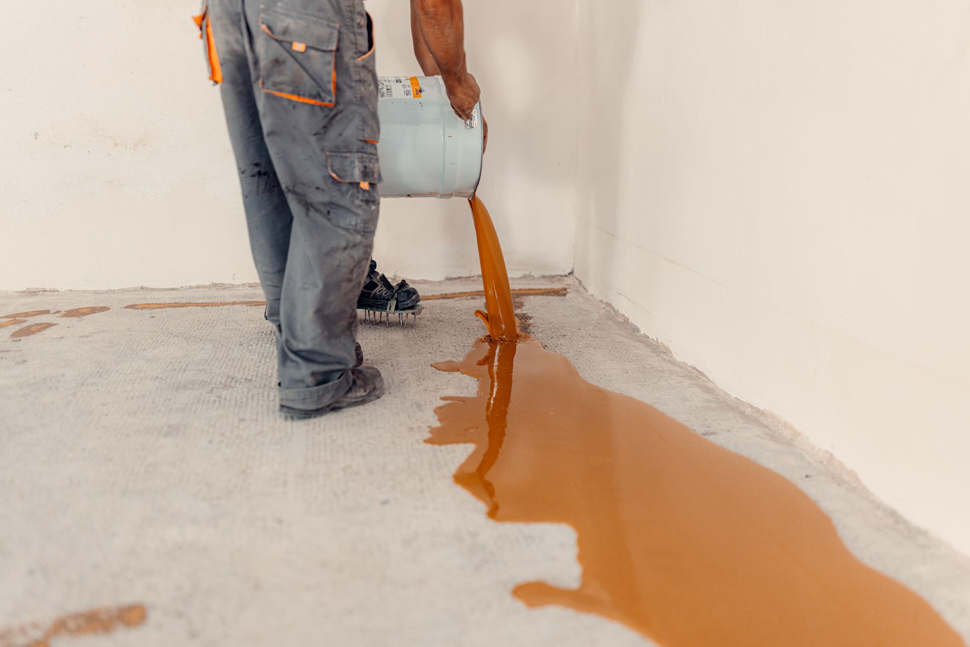 Person pouring orange liquid from a bucket onto a floor in a room.