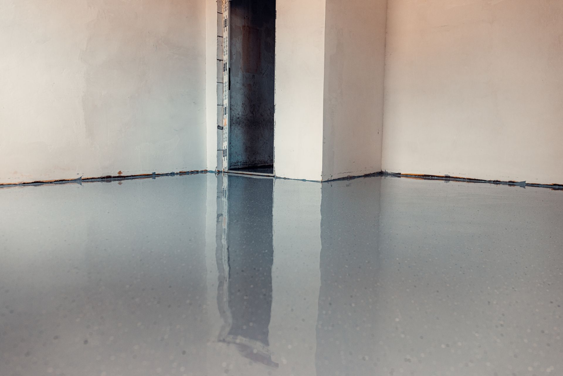 A room with newly poured, reflective gray epoxy flooring; white walls and doorway.