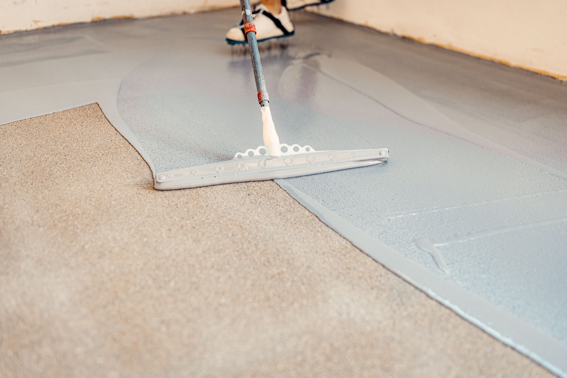 Person using a squeegee to apply epoxy coating to a concrete floor; interior.