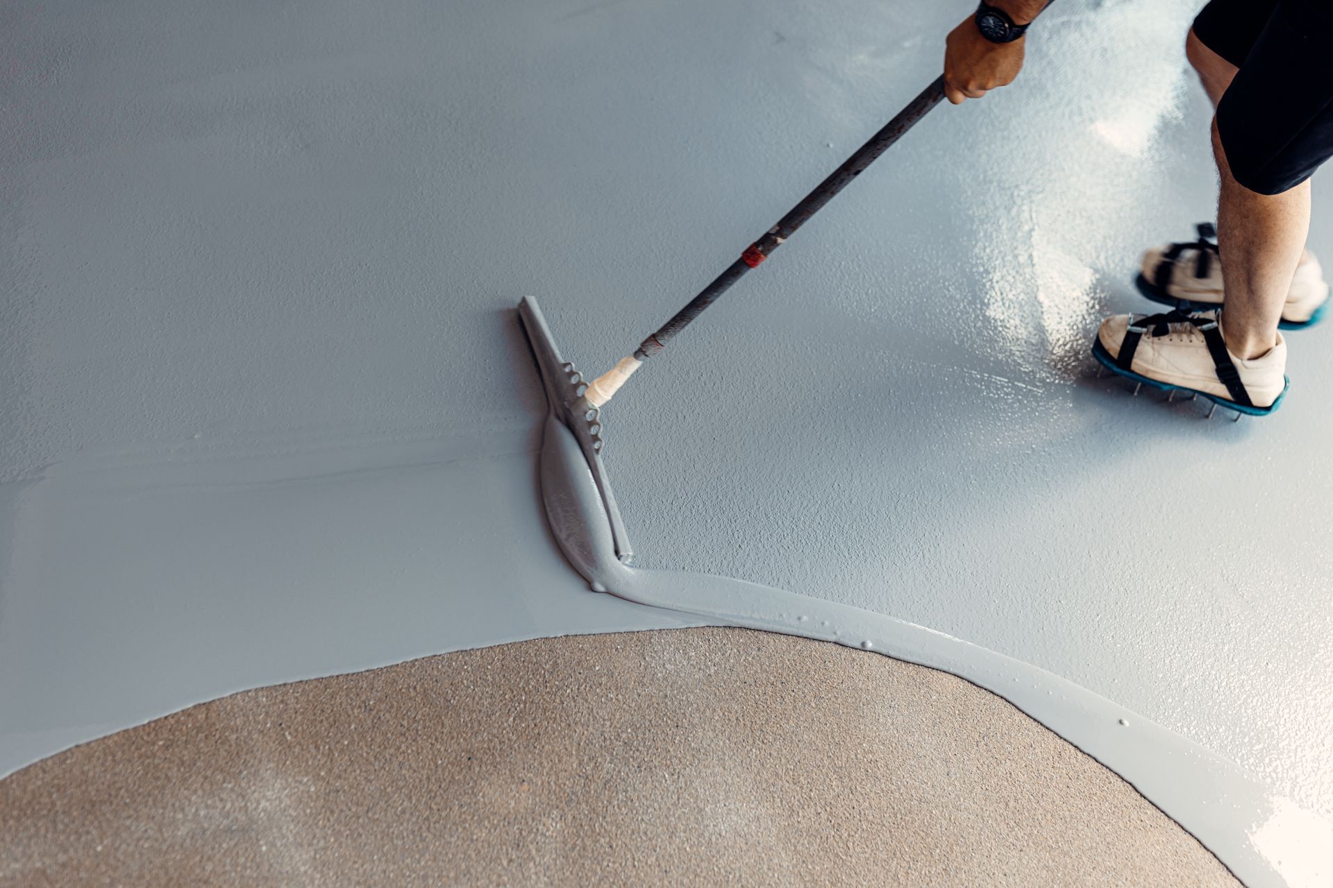 Person smoothing epoxy coating on a gray floor with a squeegee.