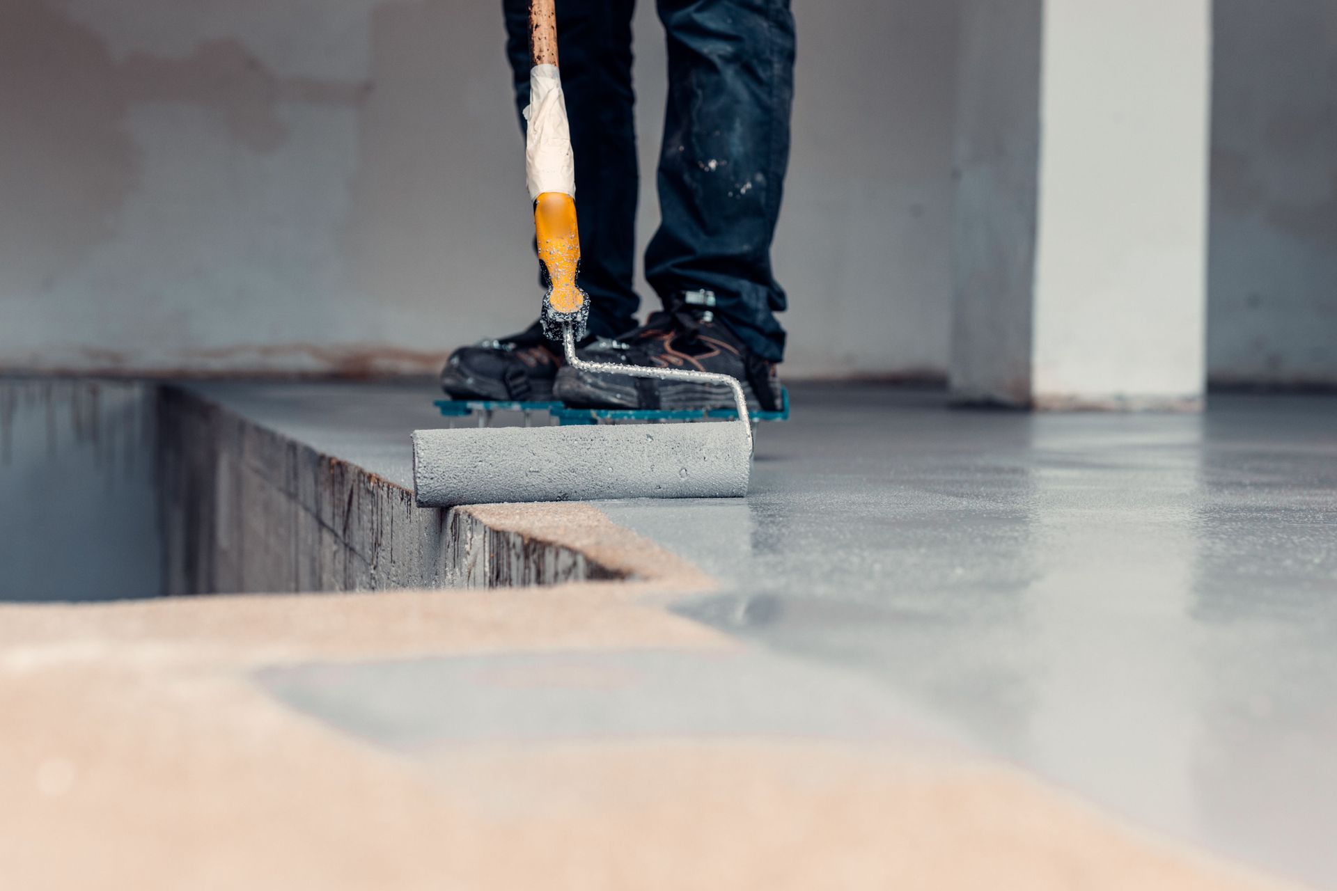 Person painting a concrete floor with a roller.