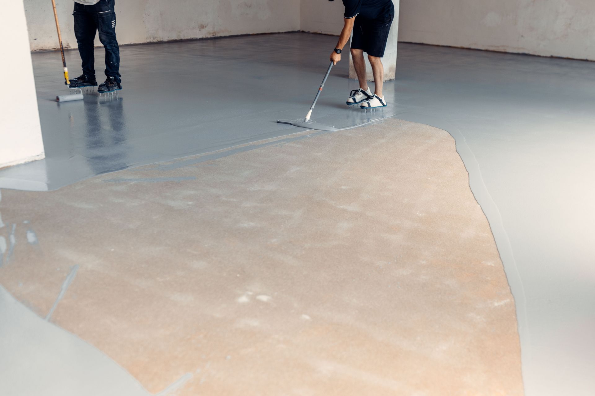 Two people applying a light gray epoxy coating to a concrete floor.