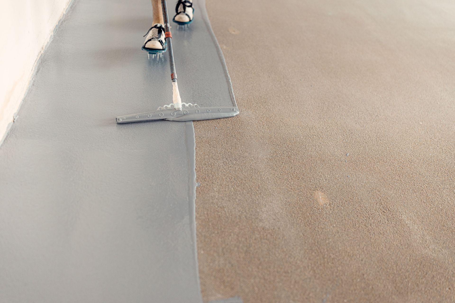 Person applying gray coating to concrete floor with a roller.