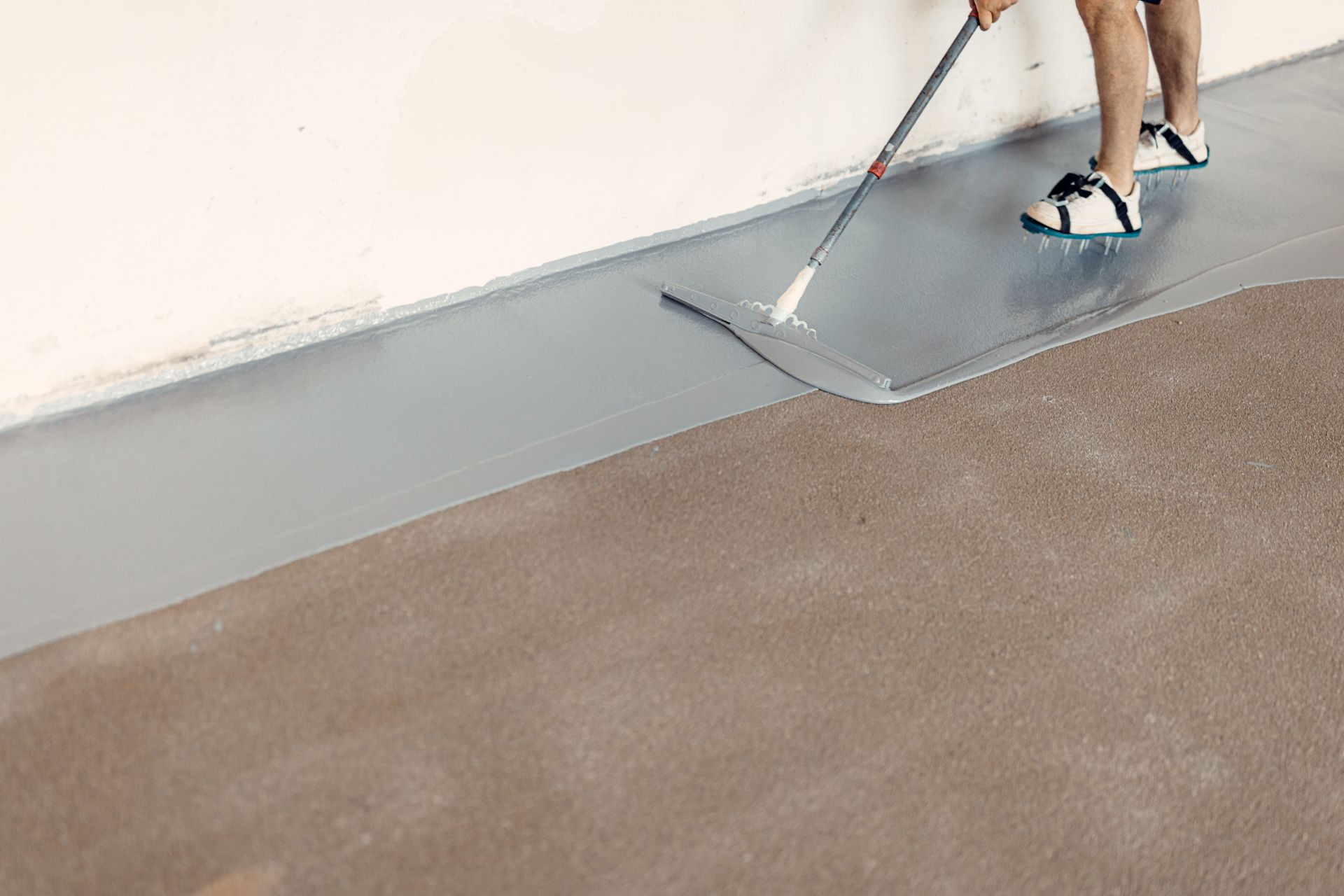 Person applying gray coating to concrete floor with a squeegee.