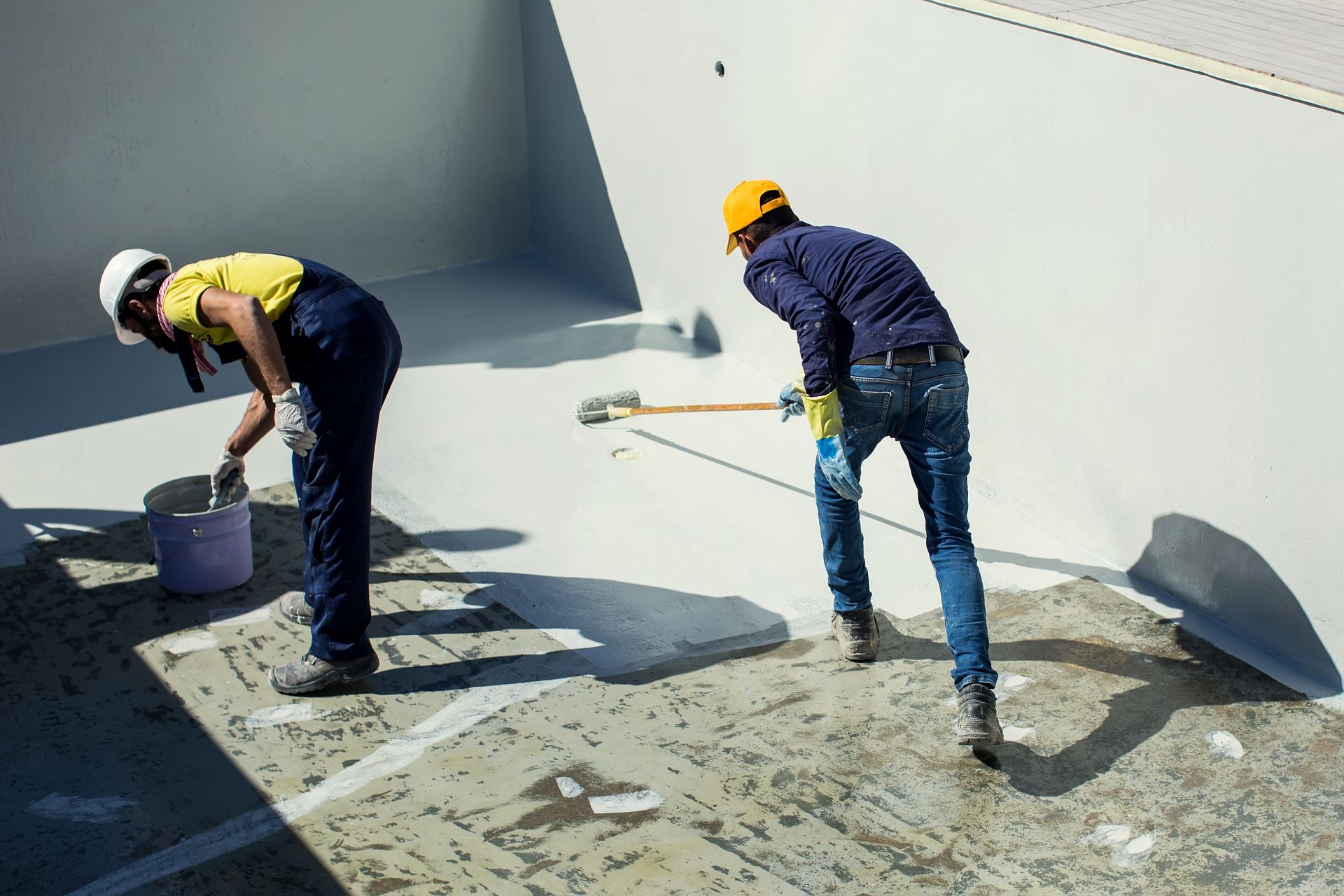 Two people painting a light-colored surface in a pool or similar structure. 