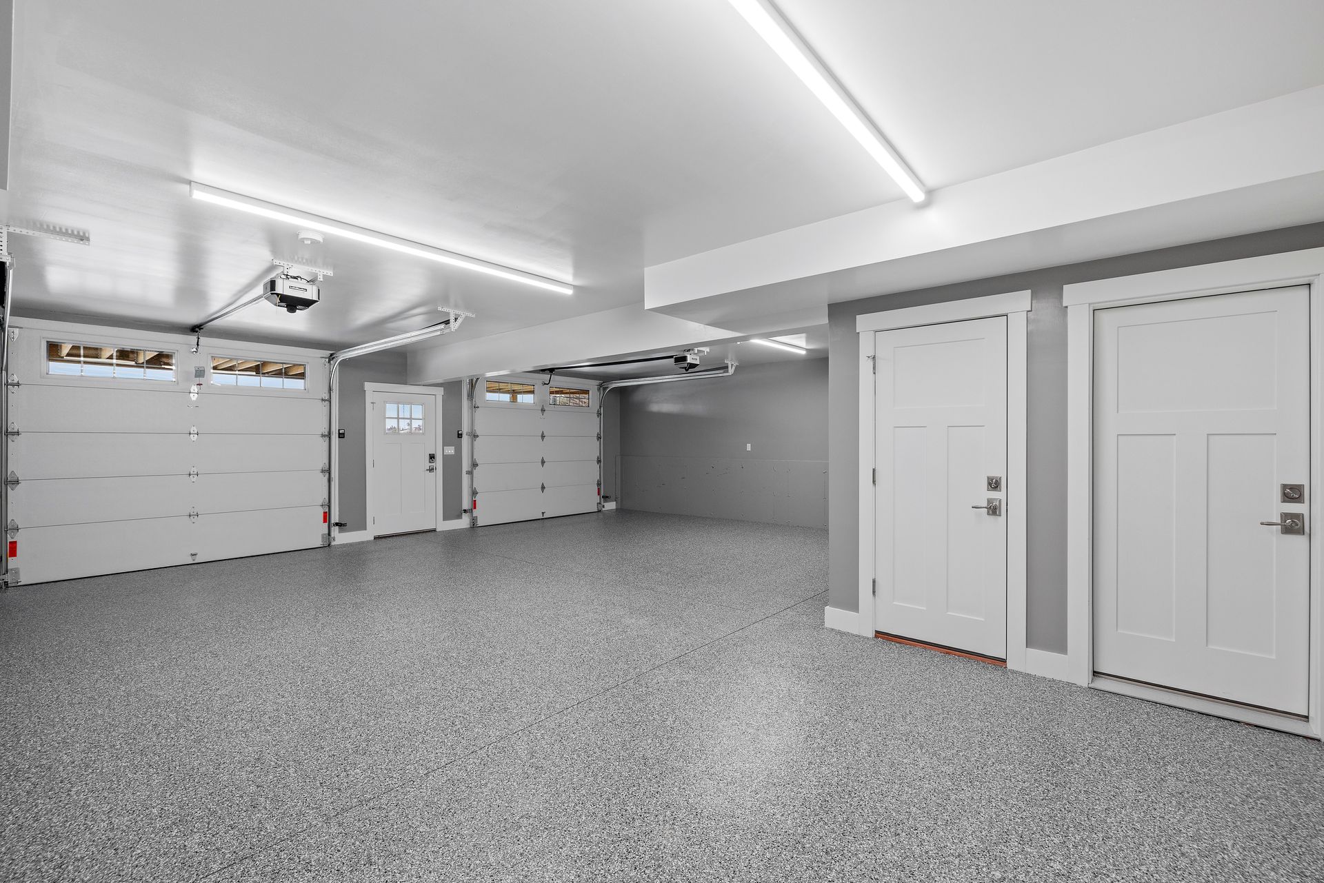 Empty, clean garage with white doors, light gray epoxy floor, and overhead lighting.
