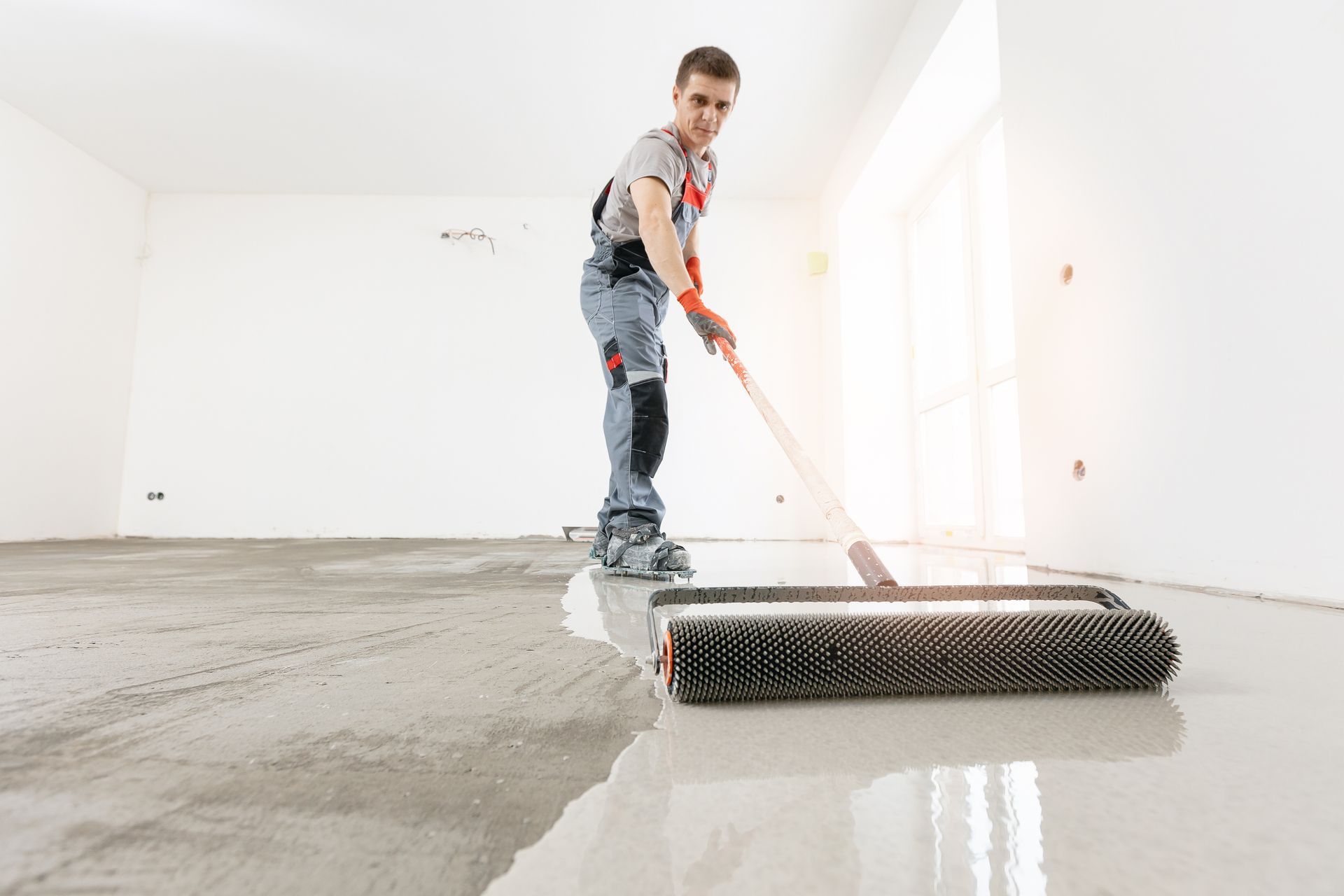 Man using roller to smooth concrete floor in a room.