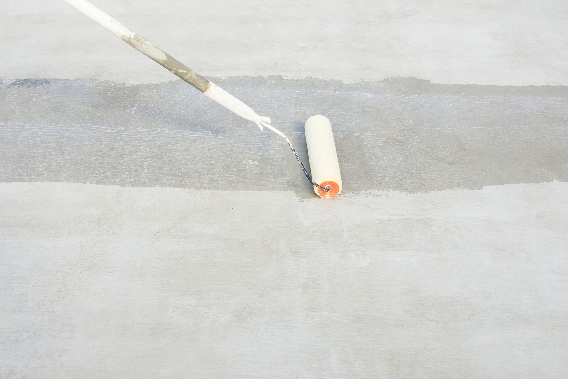 A paint roller applying a light-colored coating to a concrete surface.