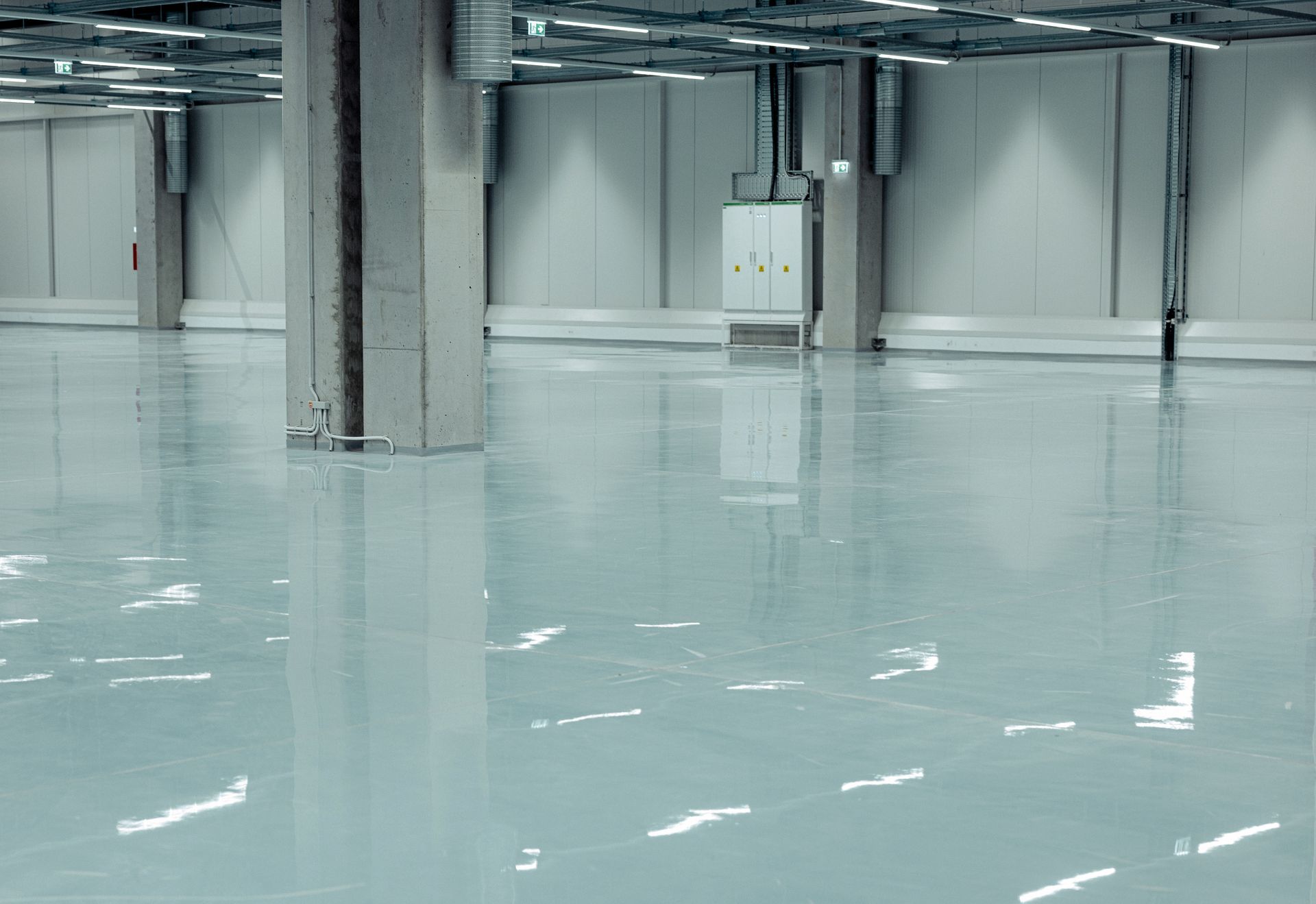 A large, empty industrial space with a shiny, light blue epoxy floor.
