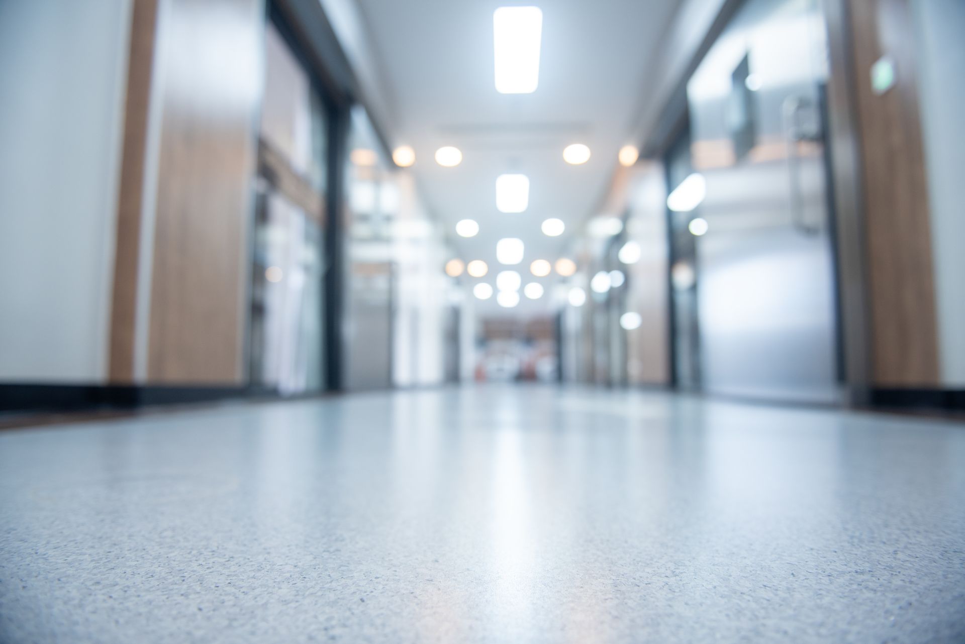 Blurred perspective of a long, light-filled hallway with closed doors and a shiny floor.