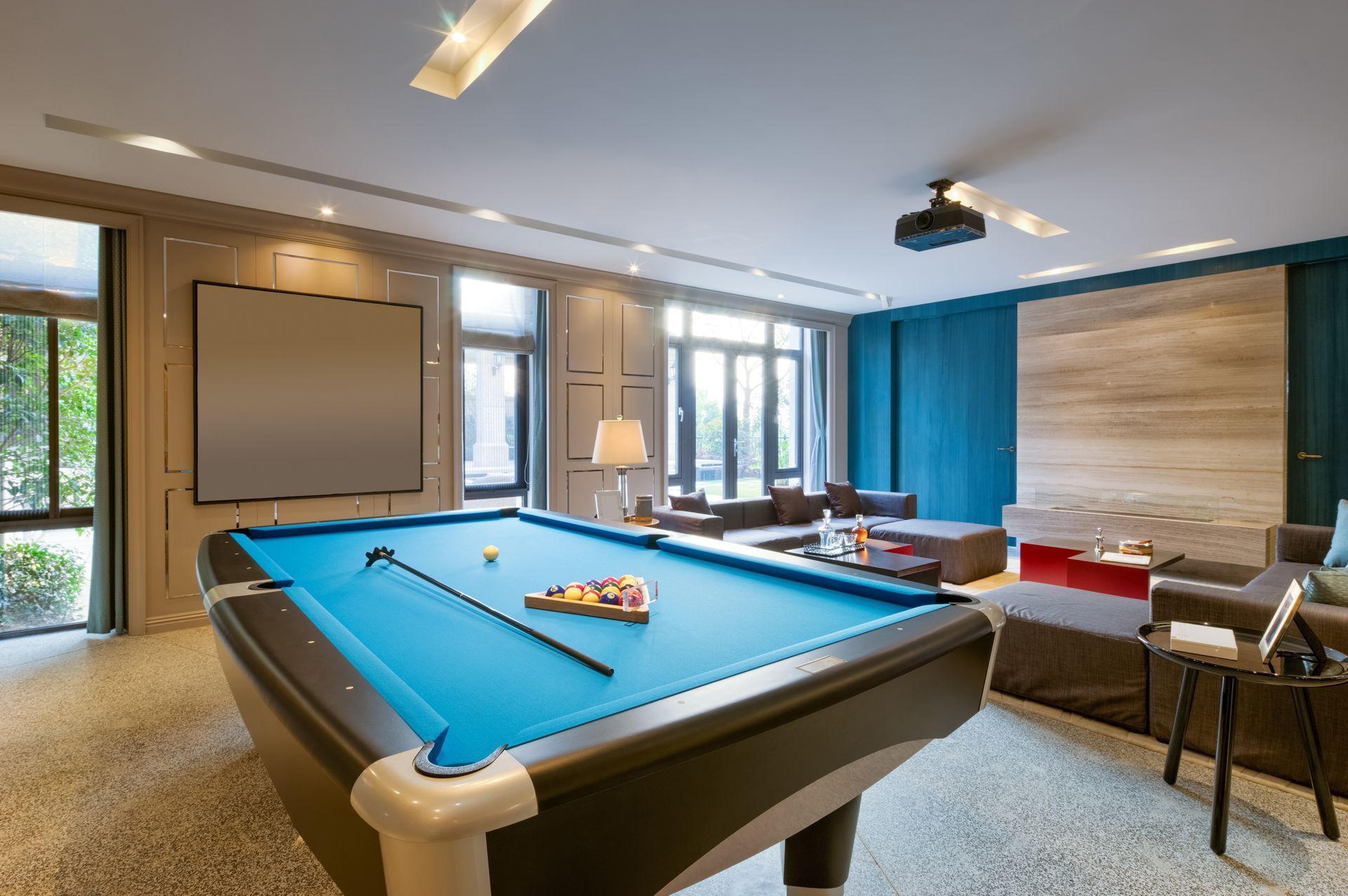 Pool table in a modern room with projector screen, blue walls, and large windows.