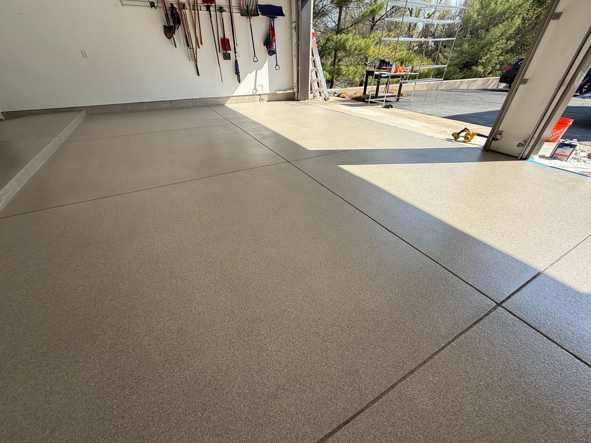Open garage with speckled concrete floor, wall-mounted tools, and sunlight streaming in from outside.