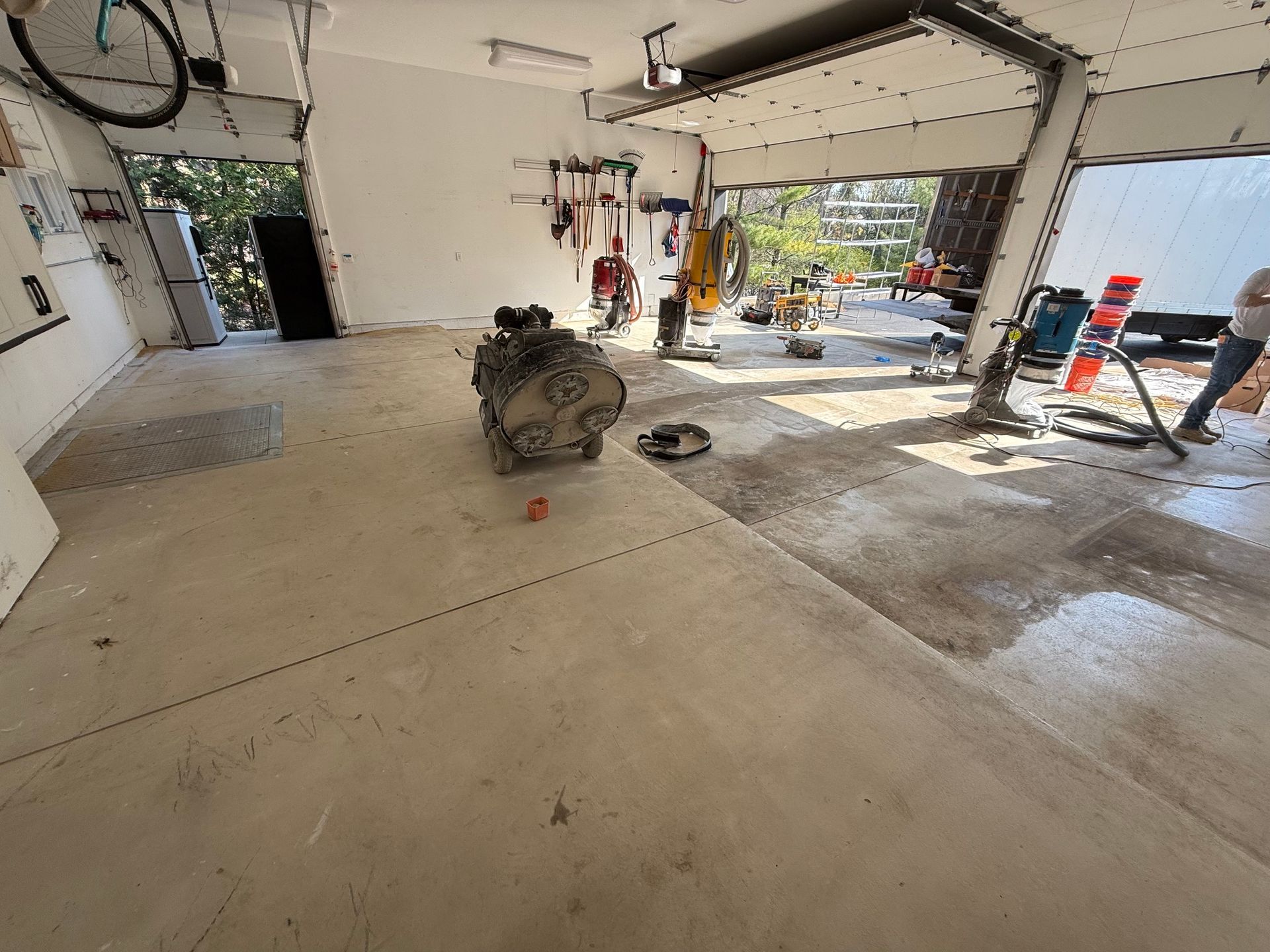 Garage with concrete floor, a dirt bike in the center, and tools and clutter near an open doorway.
