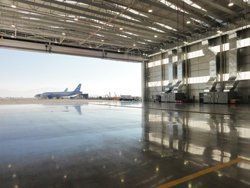 Interior view of an airplane hangar with a large open door revealing an airplane on a tarmac.