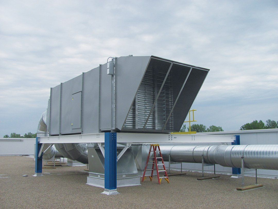 Rooftop HVAC unit on a support structure with a metal enclosure and ductwork; a ladder is present.