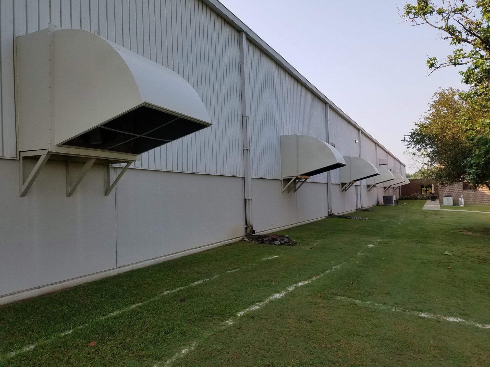 Exterior of a white industrial building with several large, hooded ventilation units. Green grass in foreground.
