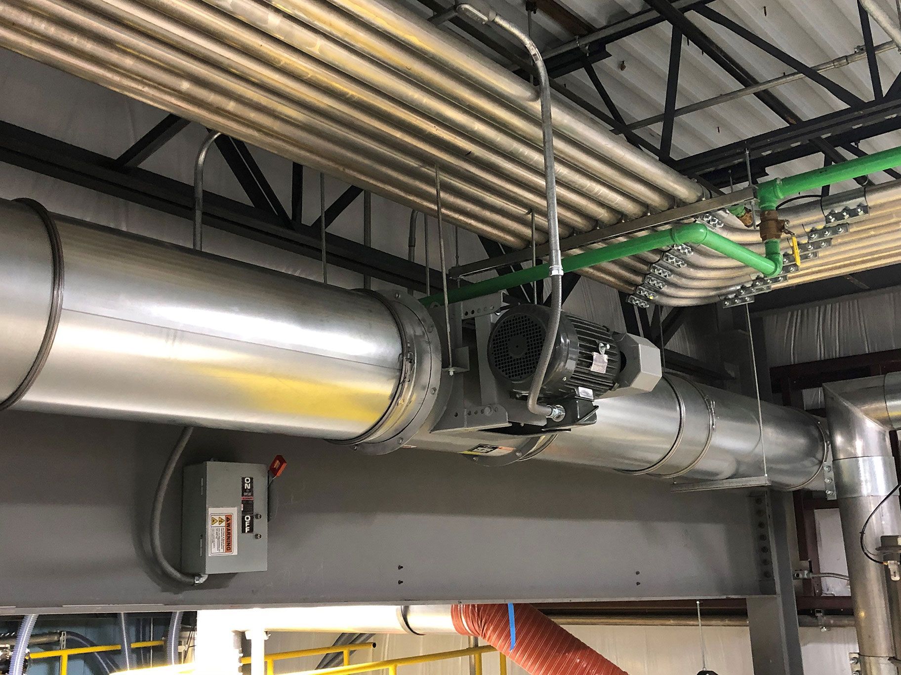 Pipes and a motor in an industrial setting, with silver insulation and green pipes overhead.
