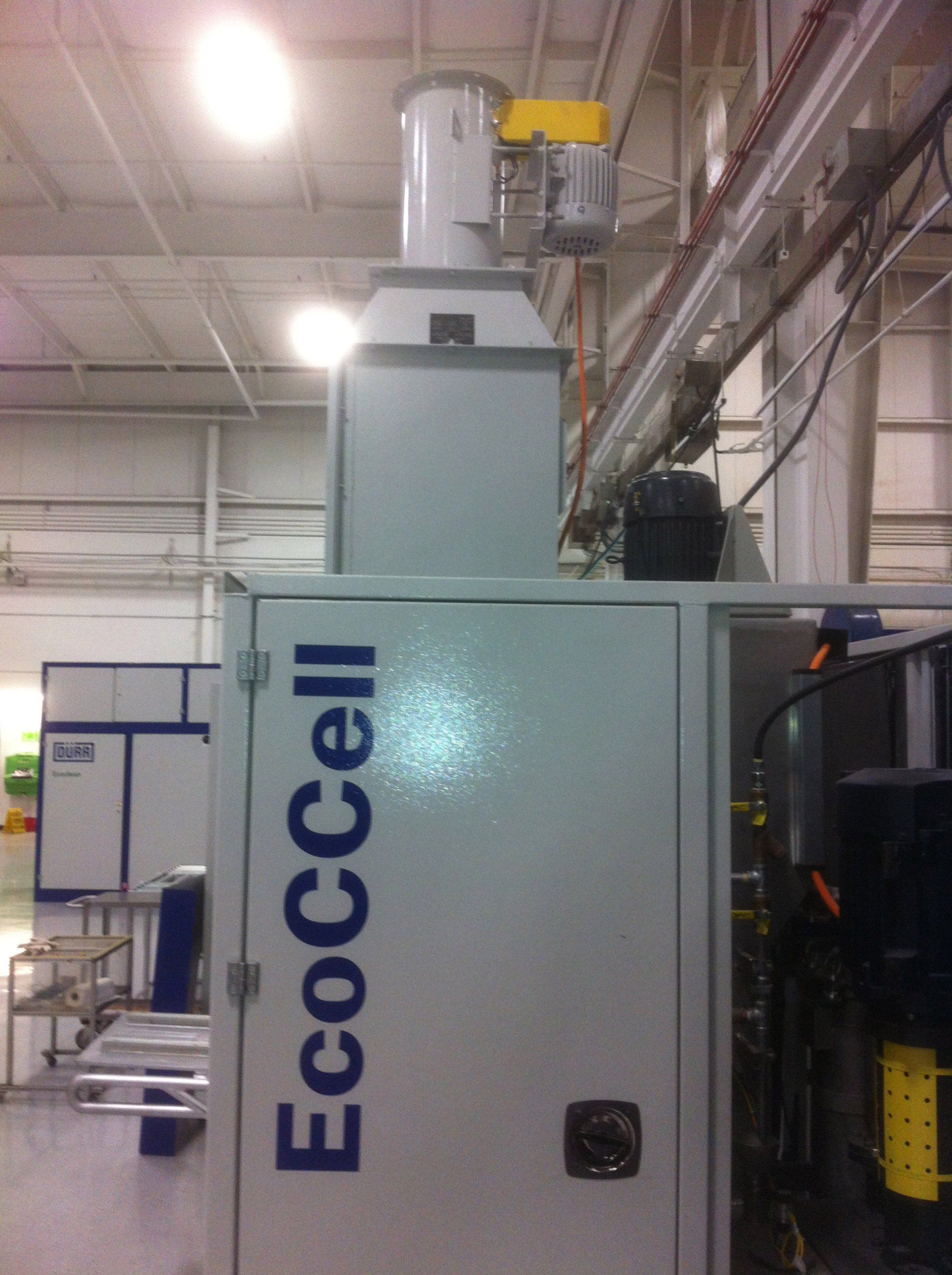 A white EcoCCell machine in a factory setting with an exhaust system, illuminated by overhead lights.