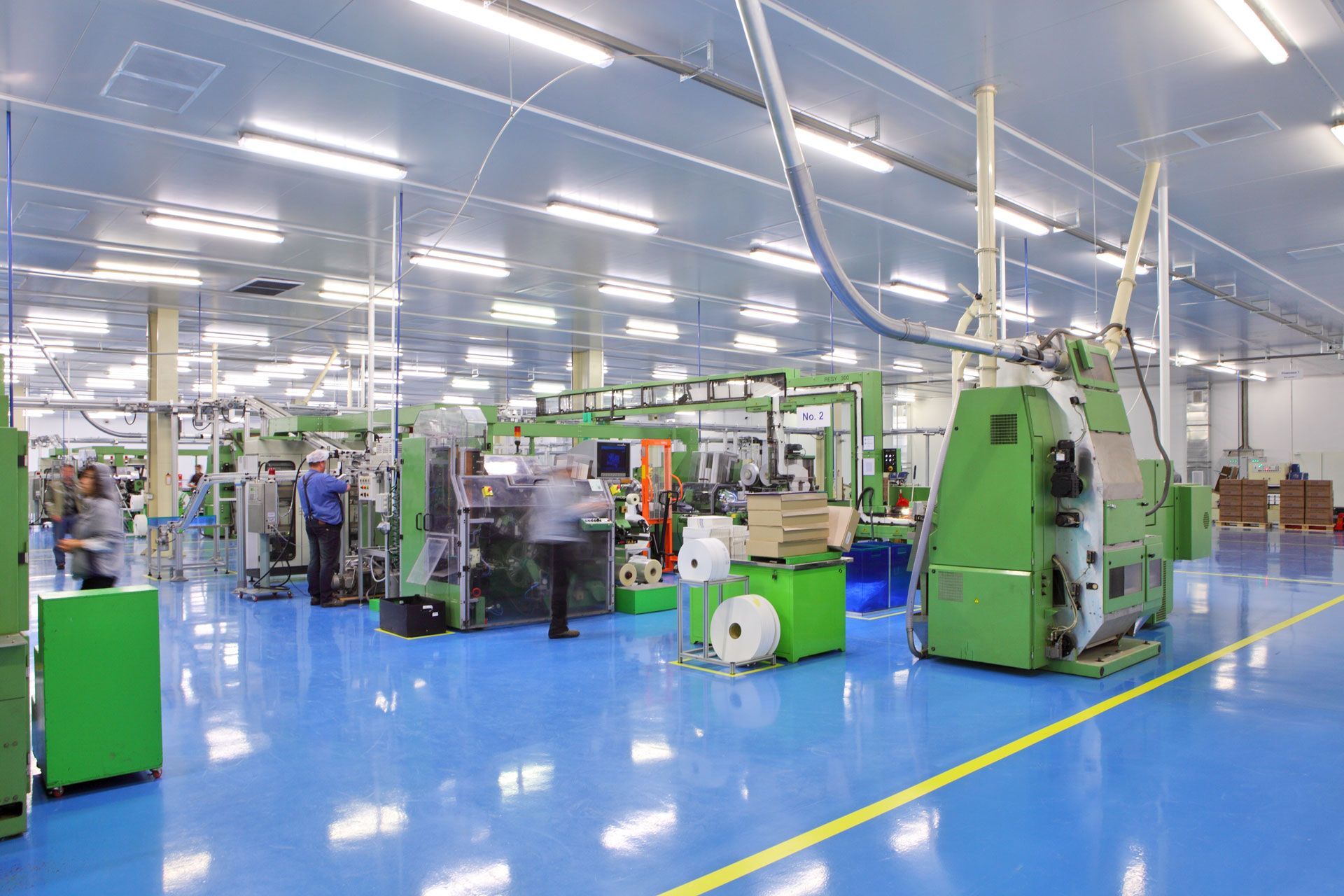 Factory interior with machinery, workers, and blue floor.