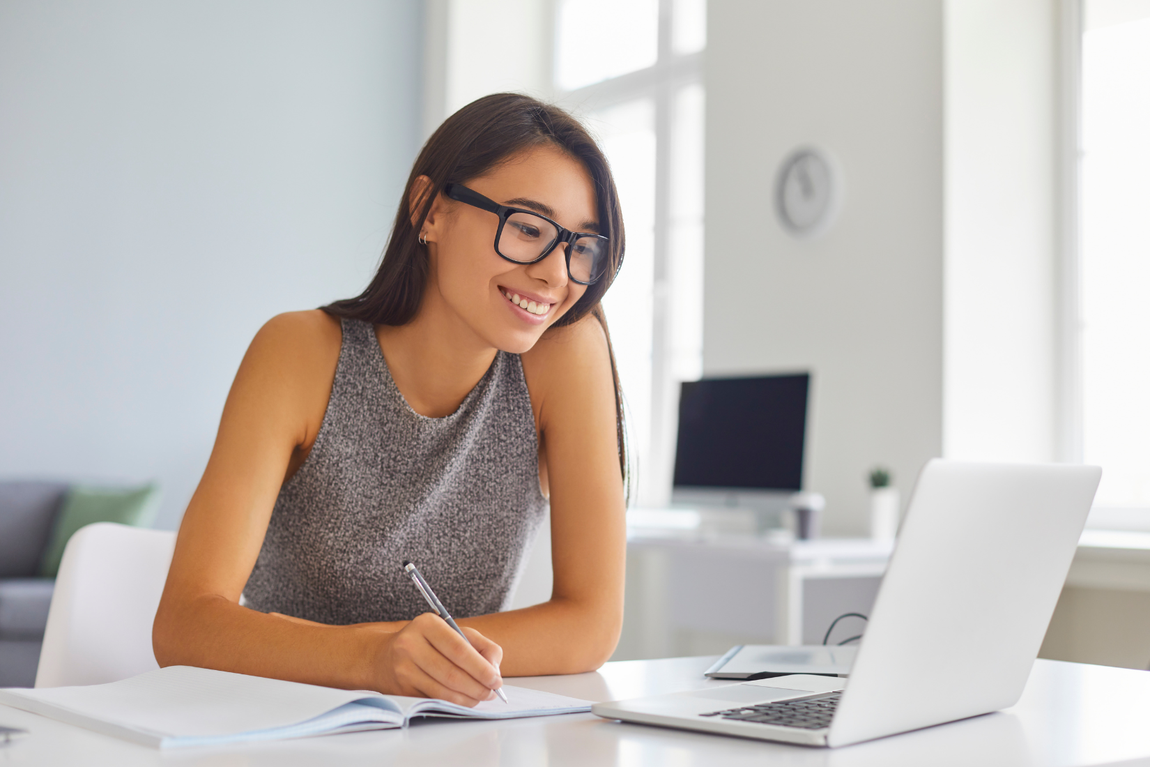 A woman is sitting at a table with a laptop and a notebook.