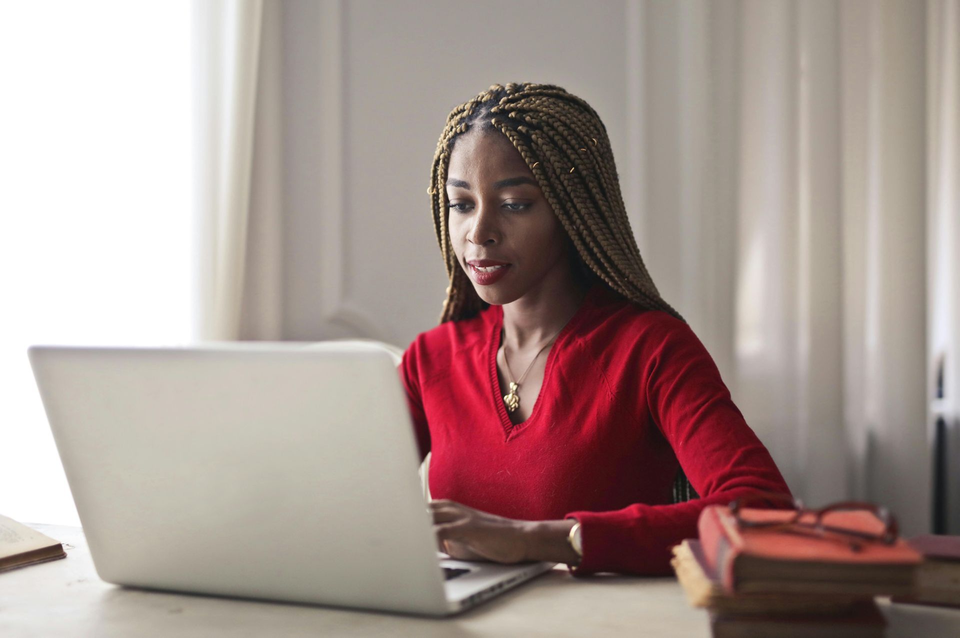 Woman in a red sweater typing on a laptop at a desk with books nearby