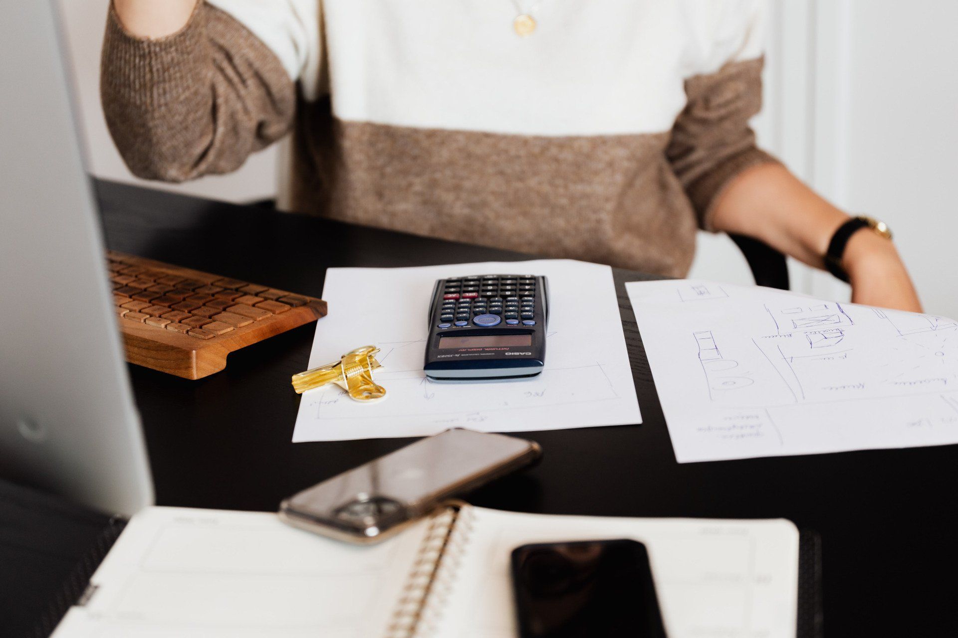 Person at desk with calculator, papers, notebook, and smartphone, working on finances or planning