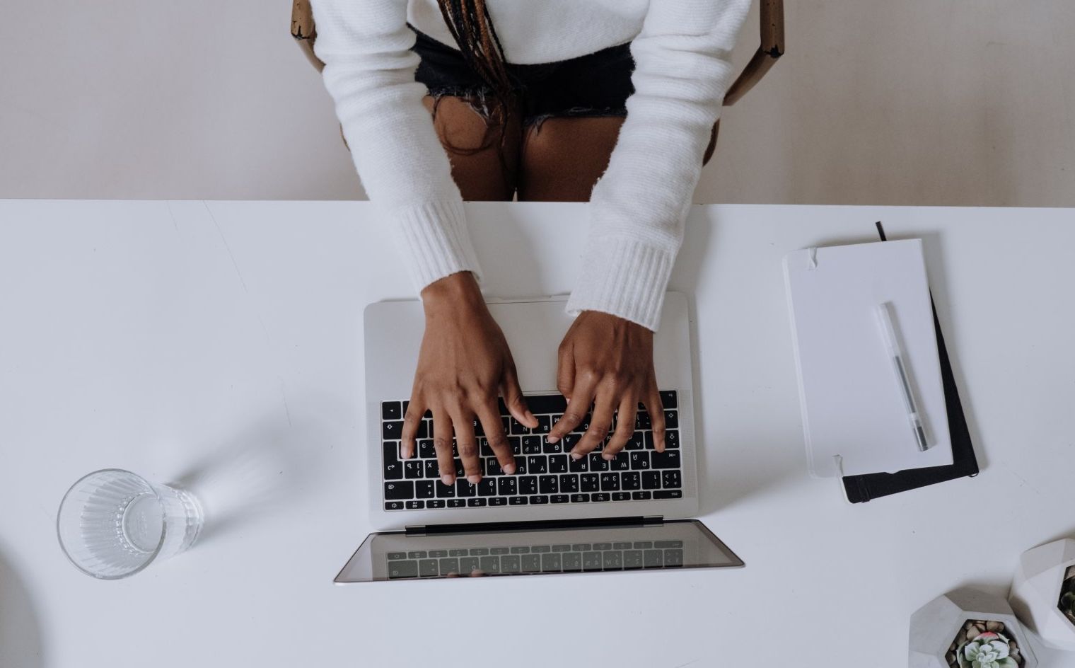A woman is sitting at a desk typing on a laptop computer.
