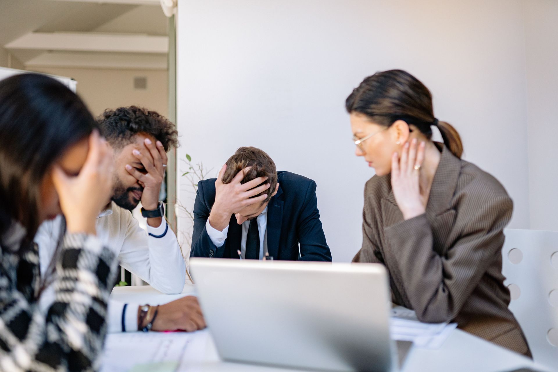 Stressed office team at a meeting table, with hands on heads around a laptop.