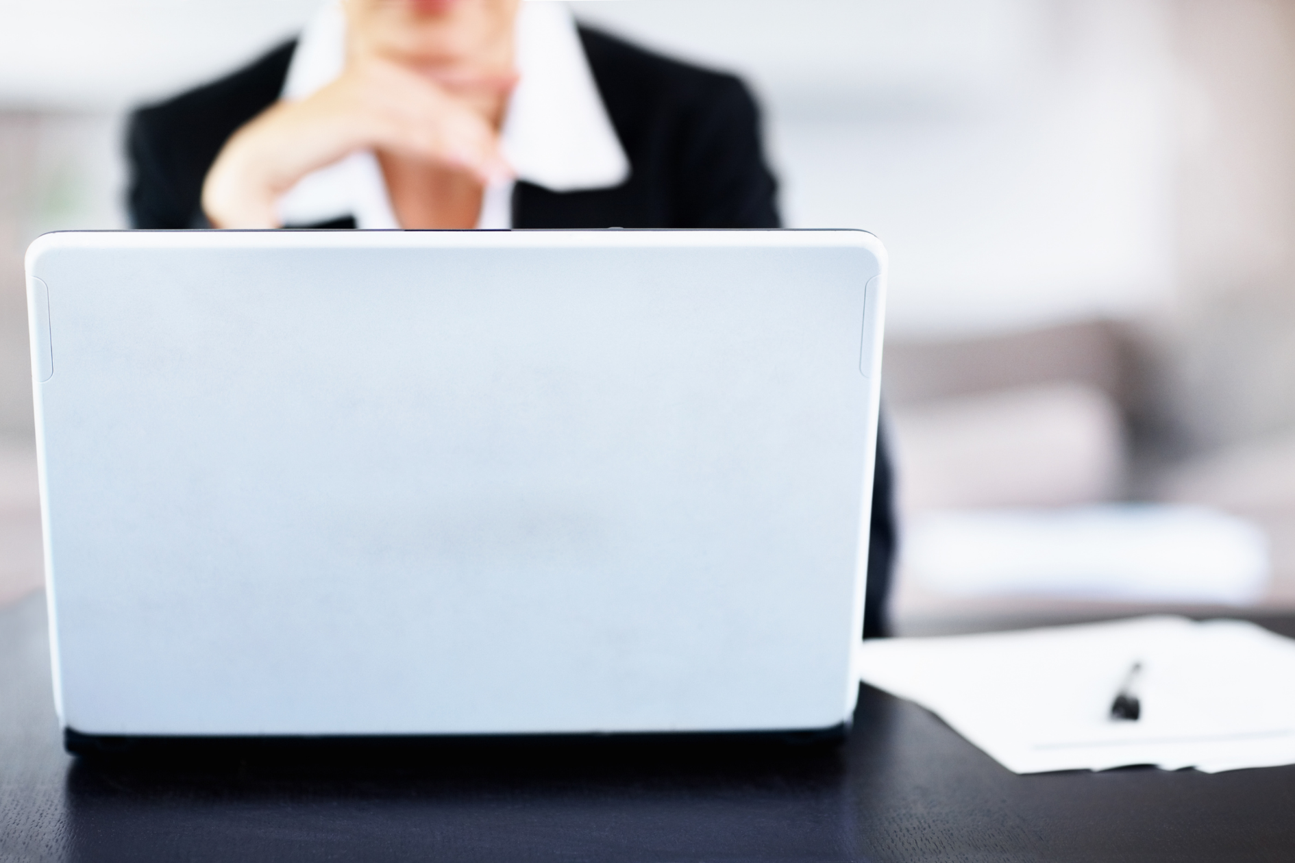 Person using a silver laptop at a desk with a pen and paper nearby