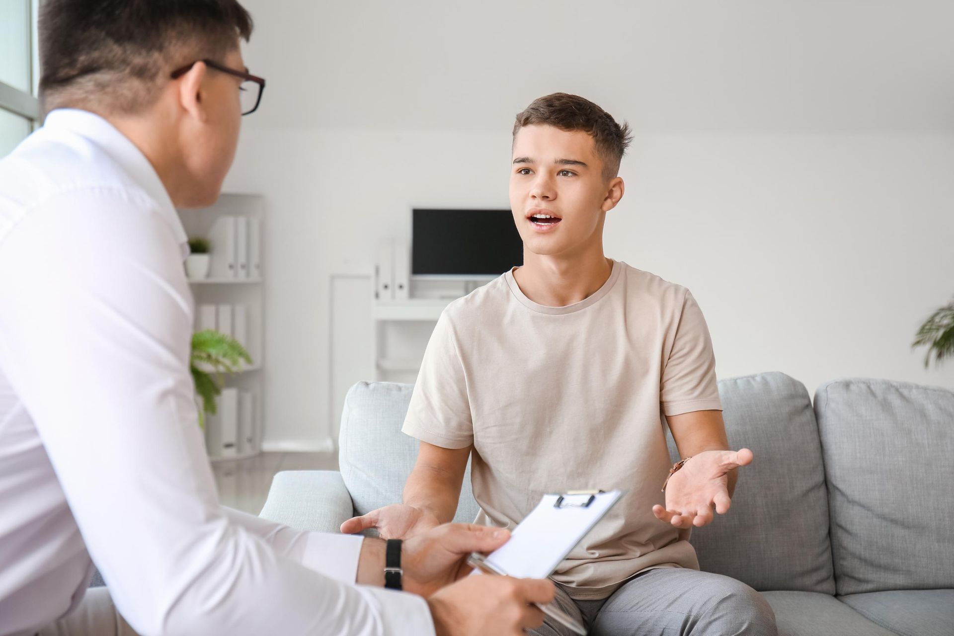 A young man is sitting on a couch talking to a doctor.