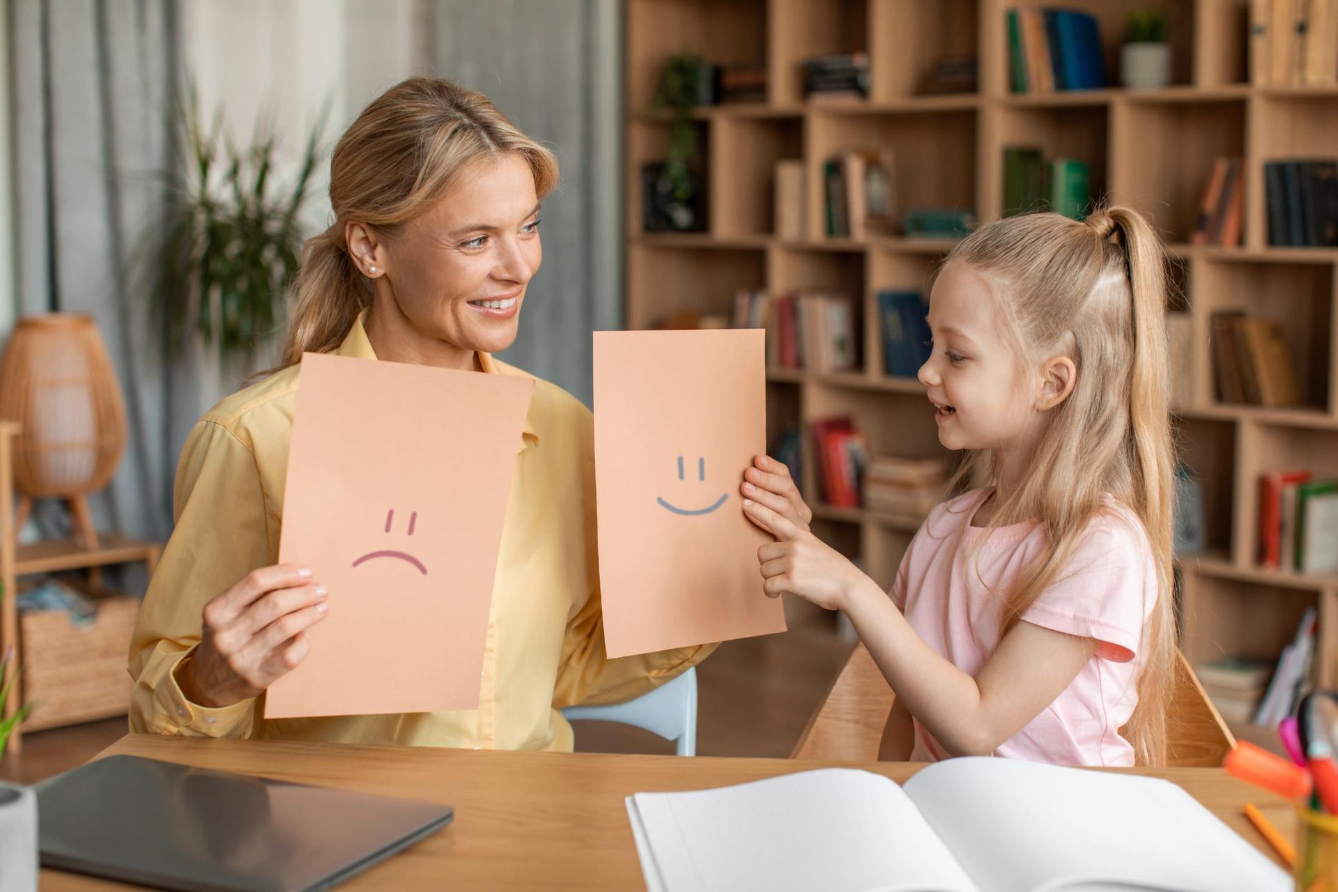 A woman and a little girl are holding cards with sad and happy faces on them.