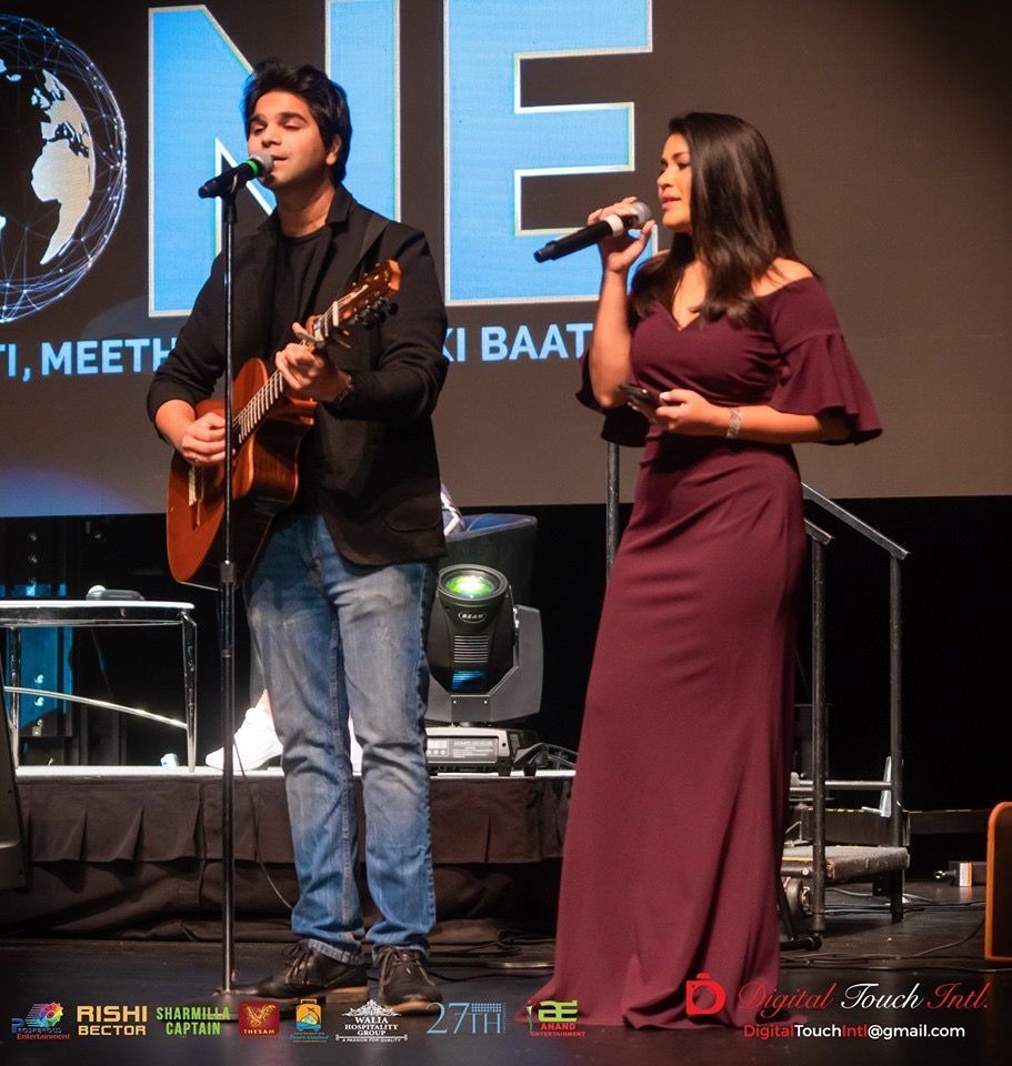 A man playing a guitar next to a woman singing into microphones