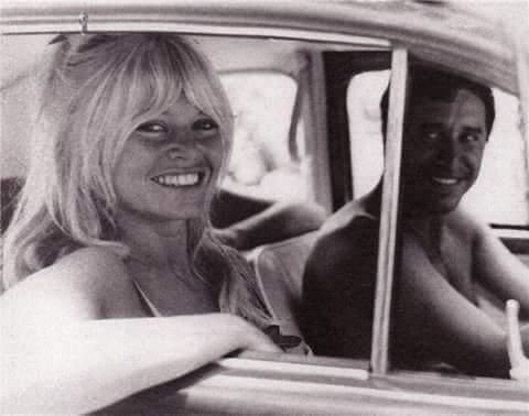Woman smiling in a car, leaning out the window next to a man. Black and white.