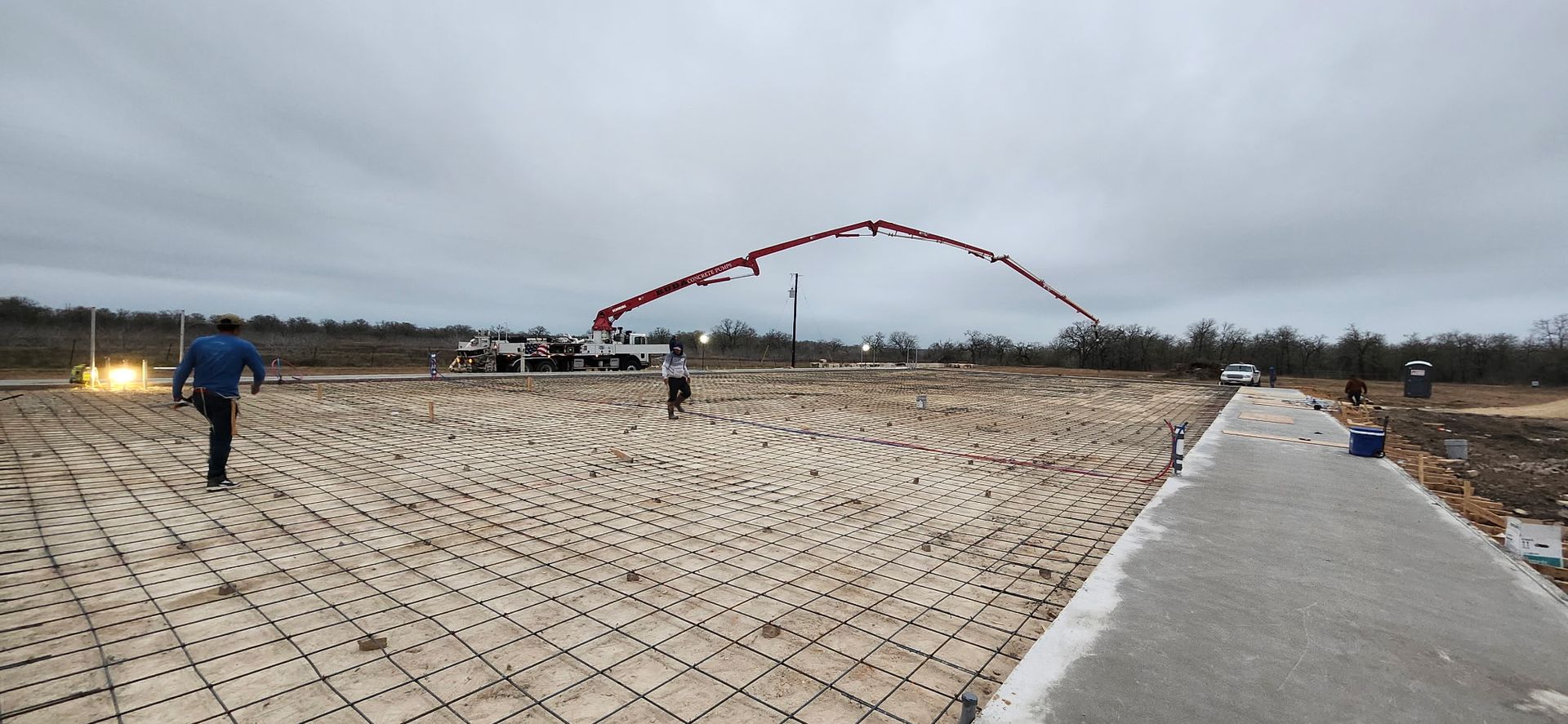 Construction site, pouring concrete. A truck with a long boom pours concrete onto rebar grid, cloudy sky.
