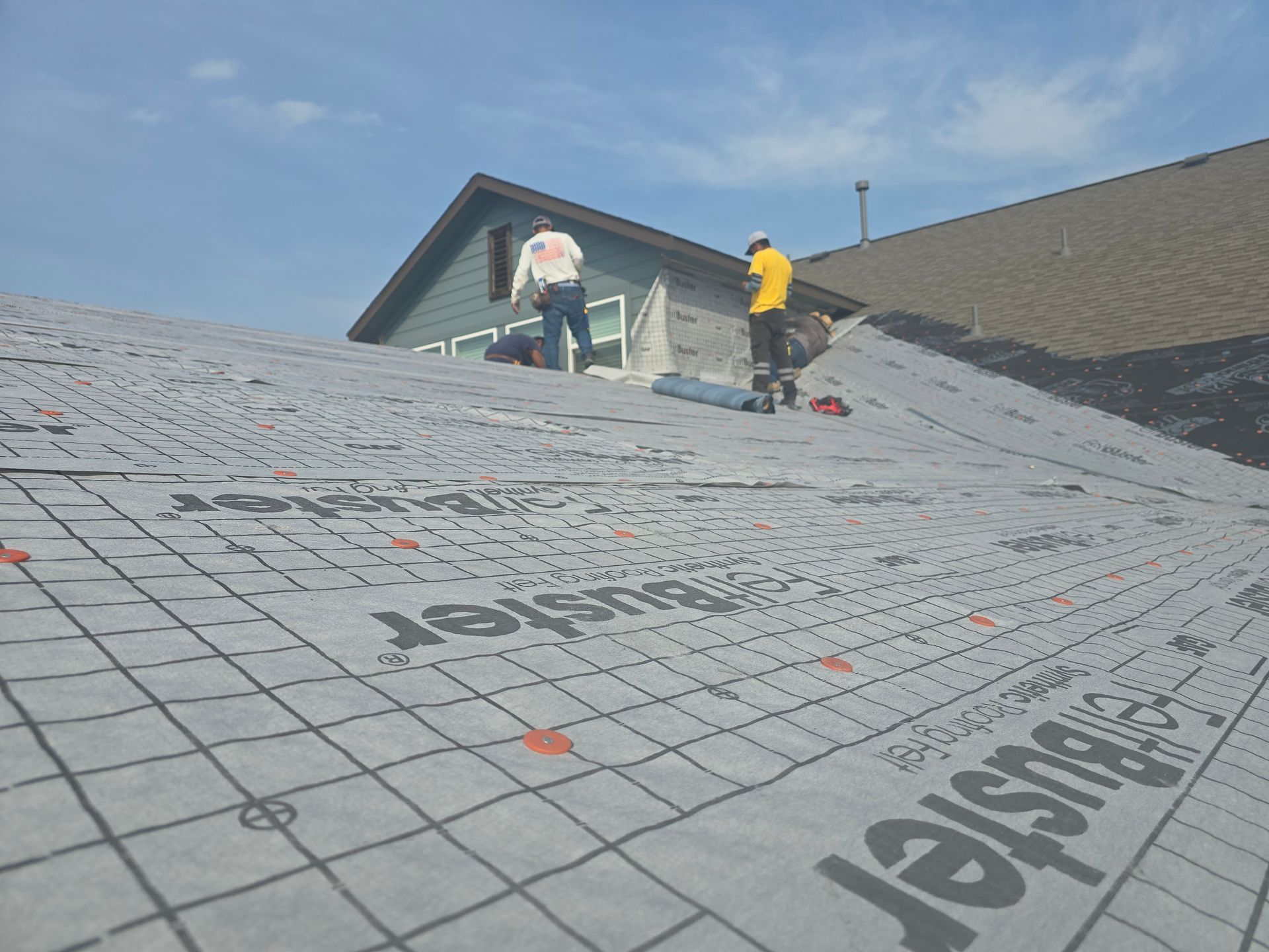 Two roofers installing roofing material on a house roof on a sunny day.