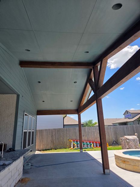 Patio with dark wood beams, light blue ceiling, concrete floor, and backyard with a pool.