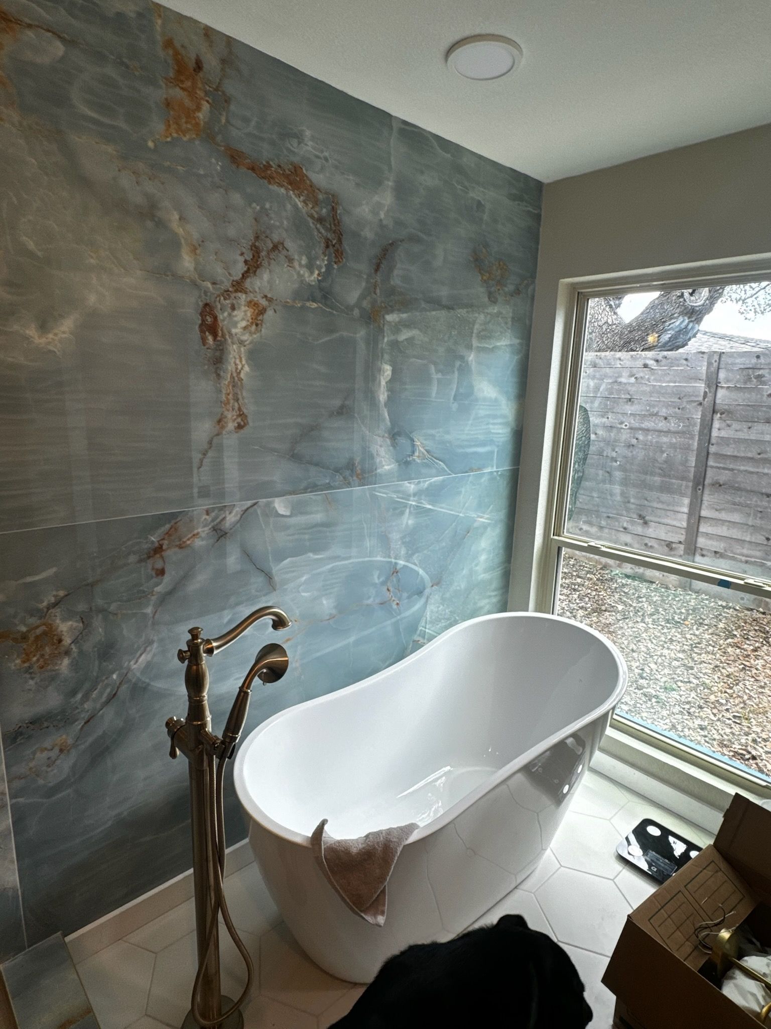 Freestanding white bathtub in a bathroom with blue marble-like tiled walls.