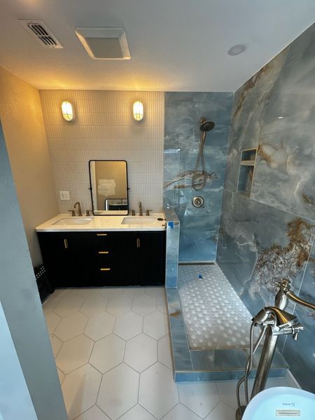 Modern bathroom with blue marble shower, black vanity, white countertops, hexagon floor tiles.