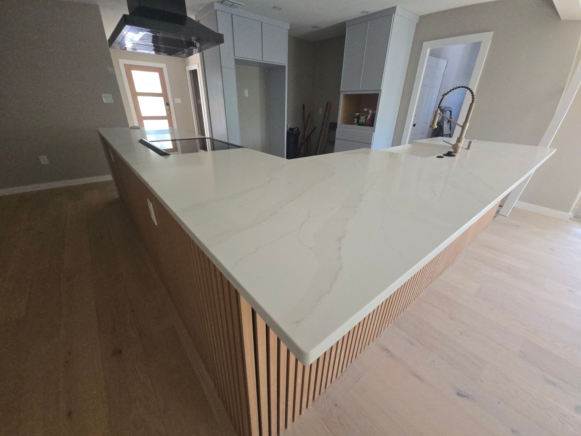 Modern kitchen with light wood cabinets, quartz countertop, and a wooden island.
