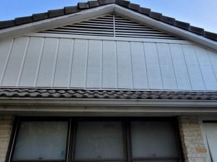 Gable roof with white siding and a vent above windows on a brick facade.