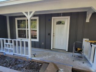 Gray house exterior with white trim, porch with white railing and door, gray siding.