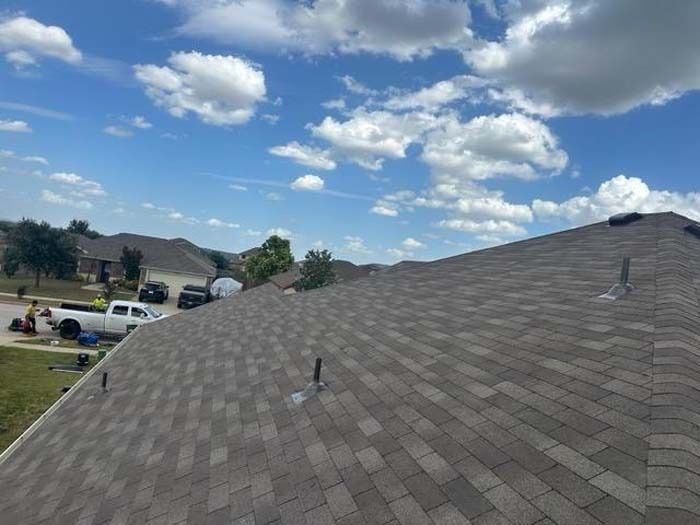 Brown shingle roof against a blue sky with clouds. People and trucks in the background.