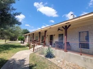 A single-story house with a long porch on a sunny day. Brown porch posts, and a concrete walkway.