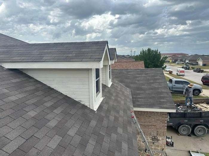 A roof being repaired, with workers on a truck in a suburban neighborhood, under a cloudy sky.