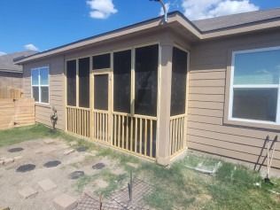 A screened porch extension on a beige house with light wood railings, door, and screens.
